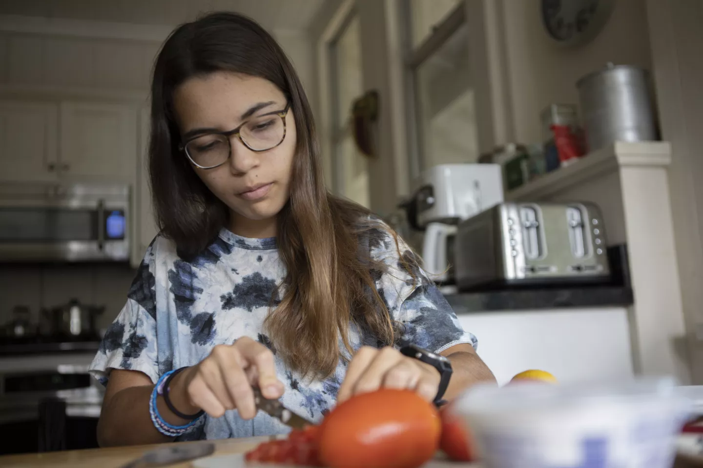 Adolescente picando tomate en su hogar, preparando una comida.
