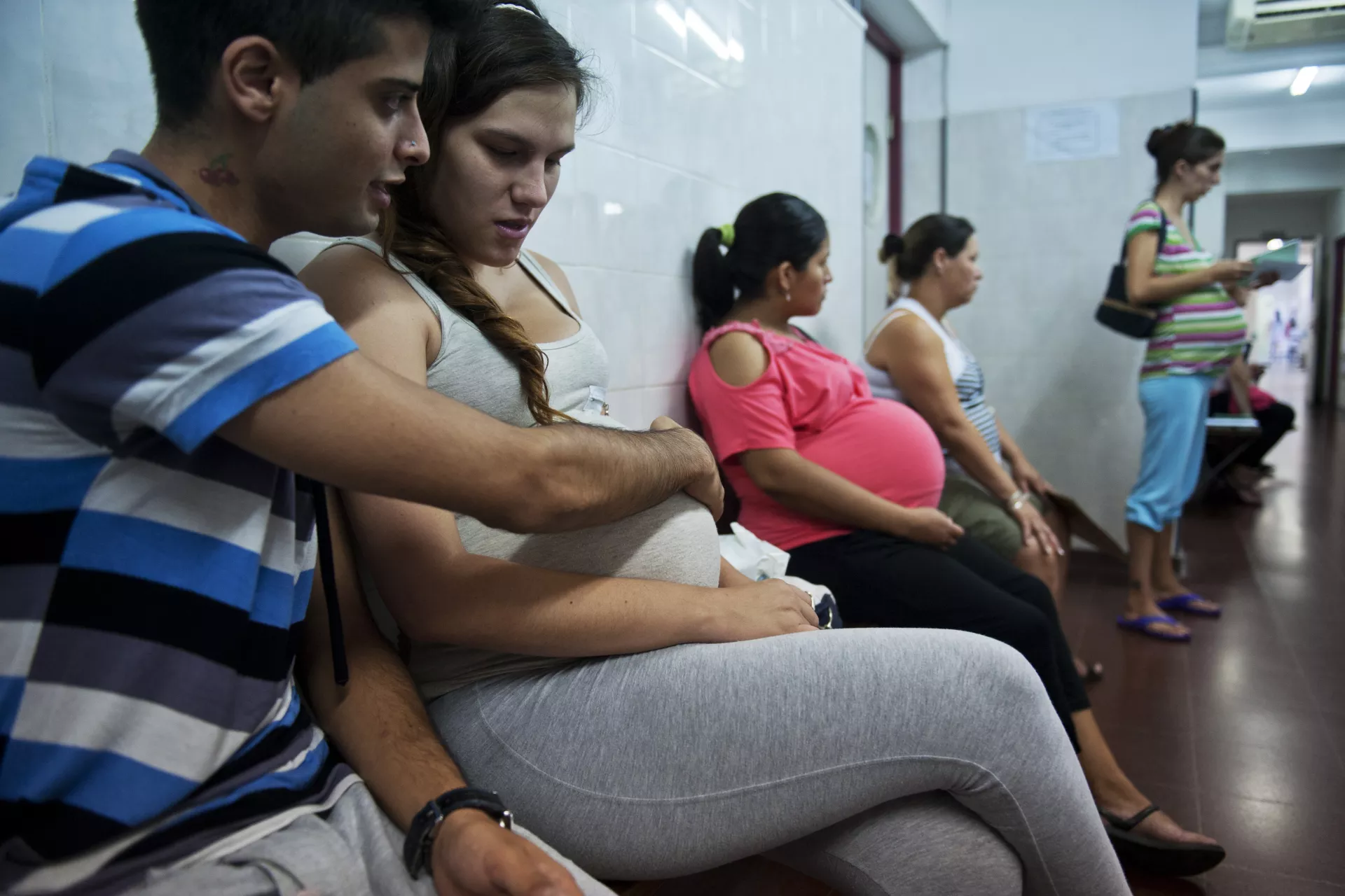 Var&oacute;n, en sala de espera de embarazadas, abrazando la panza de su pareja embarazada.