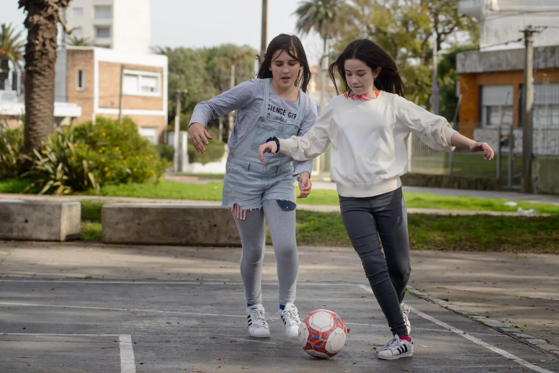 Dos adolescentes mujeres jugando al f&uacute;tbol en una plaza.