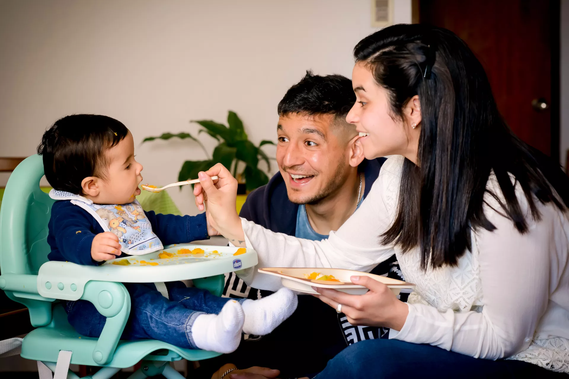 Madre y padre dando de comer pur&eacute; de calabaza a ni&ntilde;o de unos 6 meses aproximadamente.
