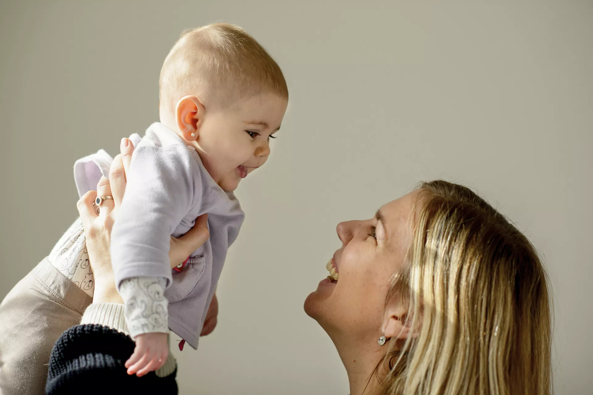 Madre sosteniendo alto a su beb&eacute; ni&ntilde;a, de unos 6 meses en brazos. Ambas se miran a los ojos.