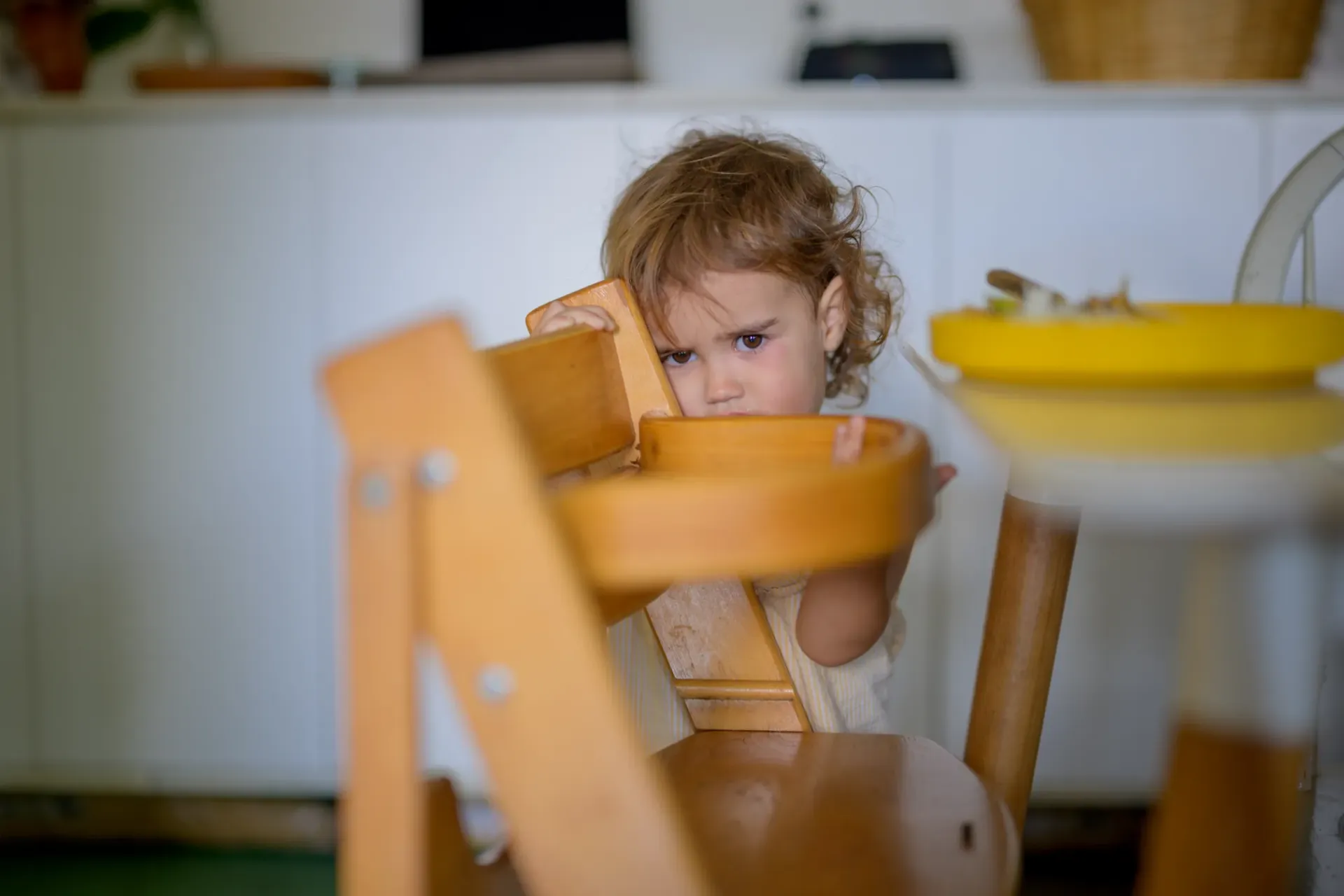 Ni&ntilde;a parada detr&aacute;s de silla de comer