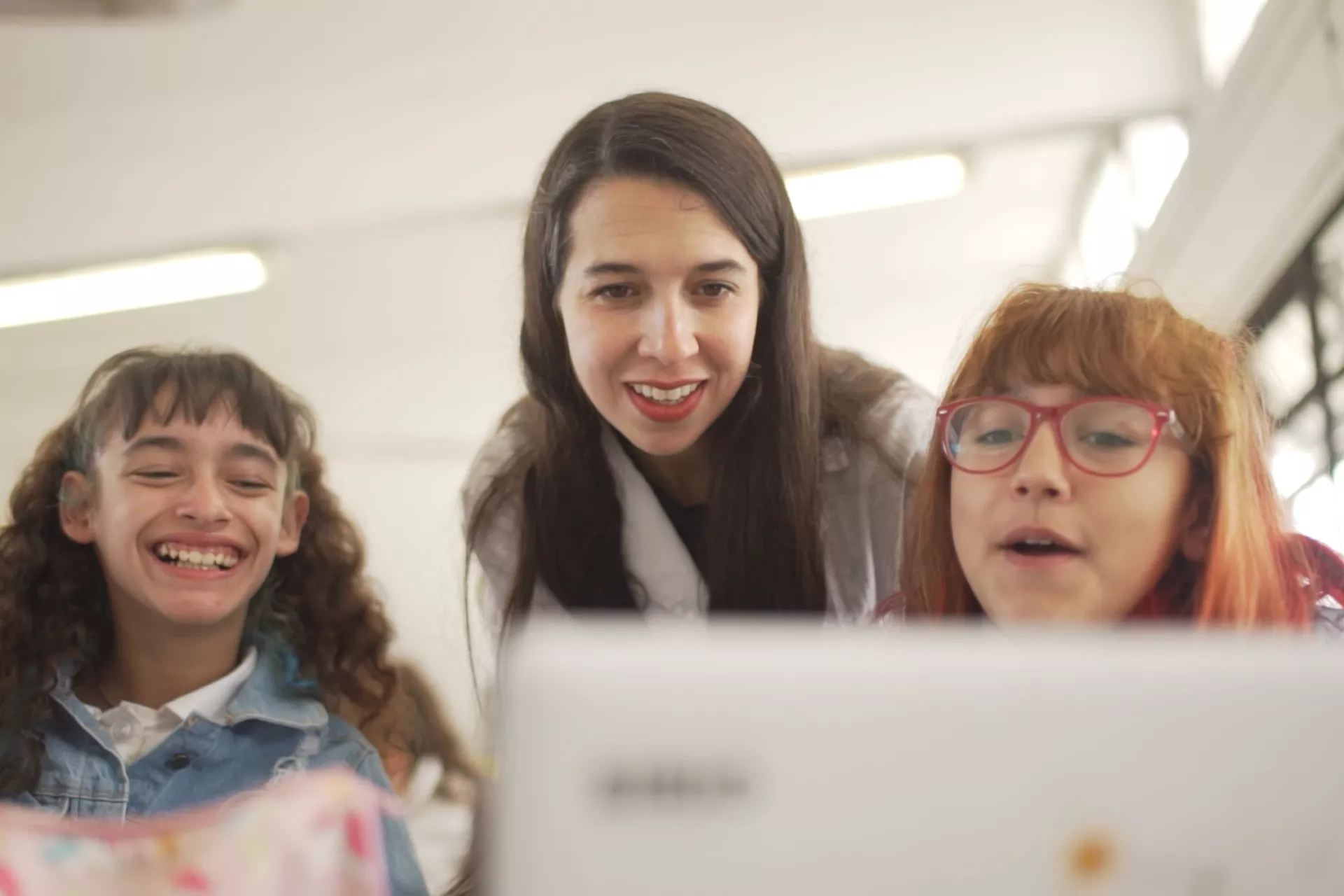 Dos adolescentes observan una tarea en la computadora junto a su docente