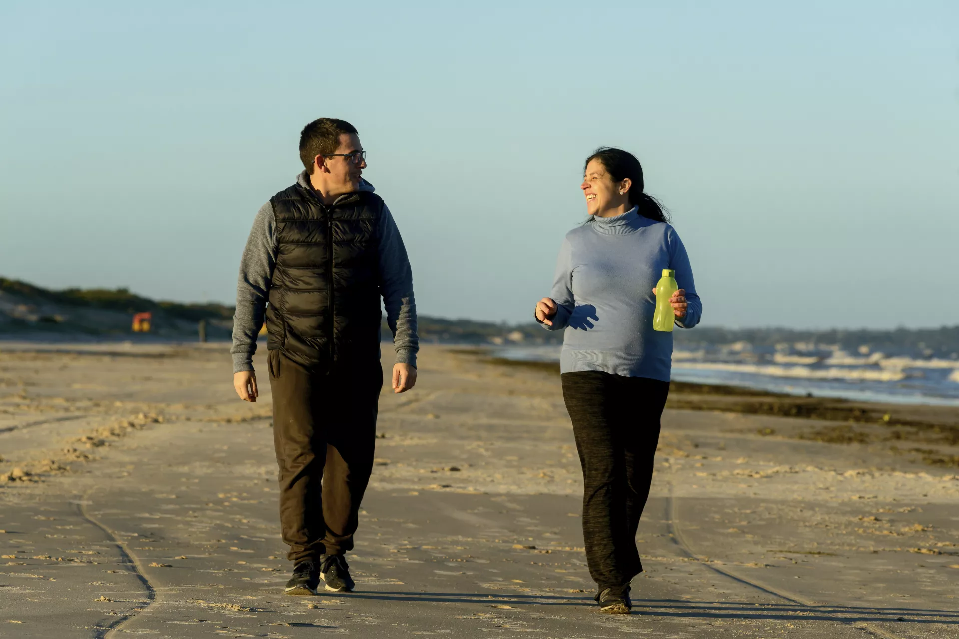 Hombre y mujer embarazada, caminando en la playa.