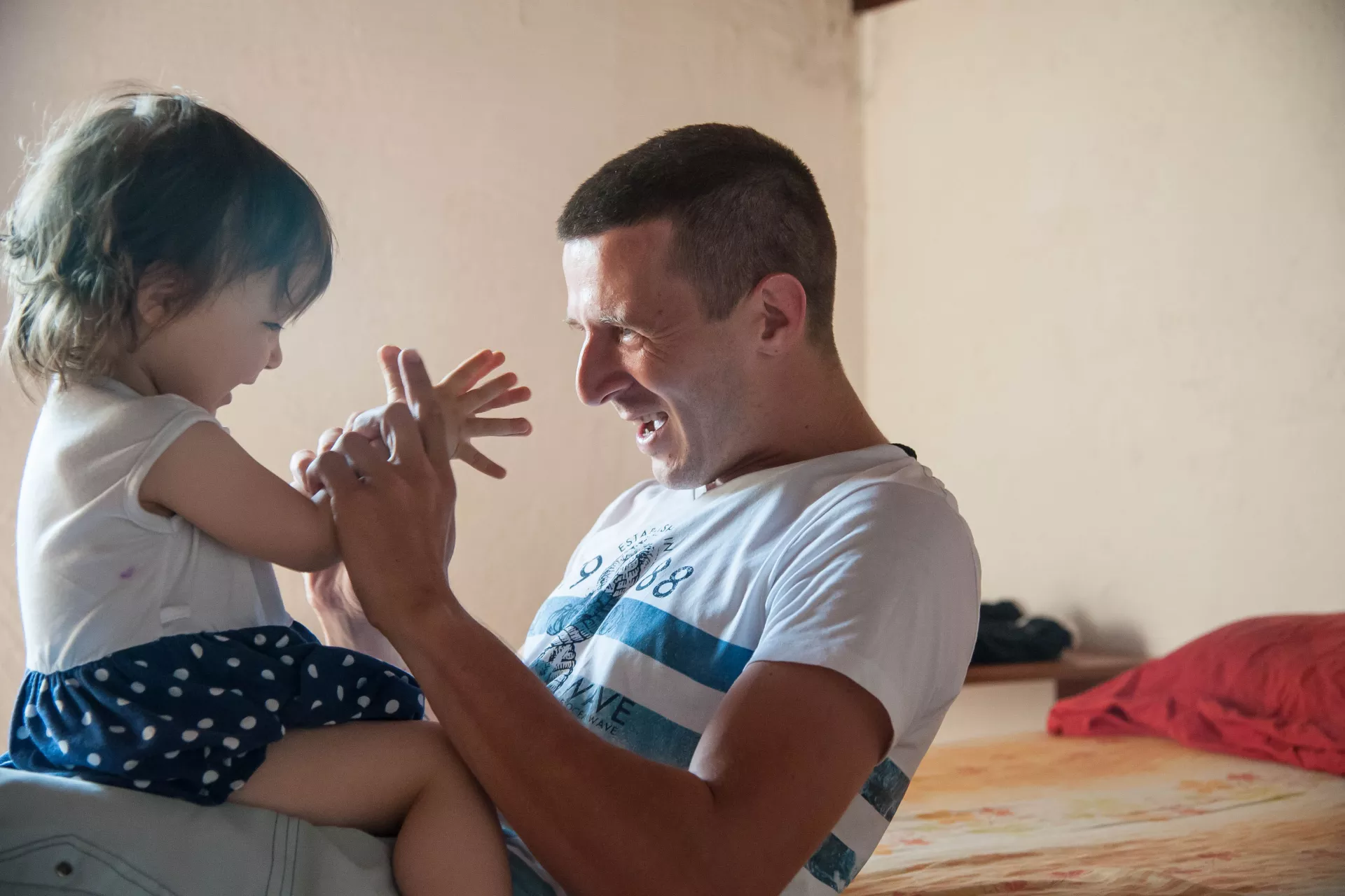 Padre, jugando con las manos de su hija, sentada en su falda, enfrentada hacia &eacute;l.