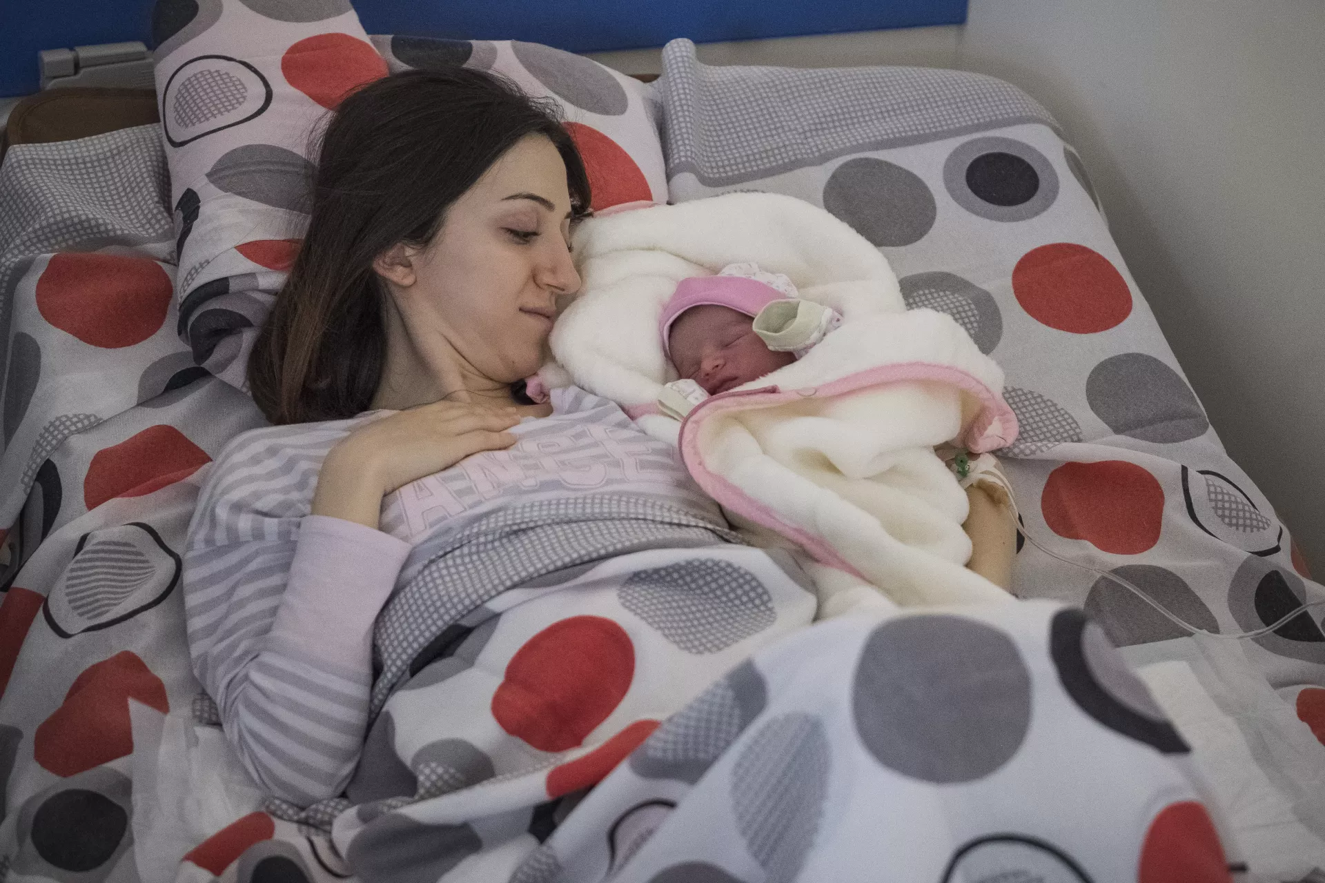 Mujer, acostada en una cama, abrazando a beb&eacute; reci&eacute;n nacido, a su lado.