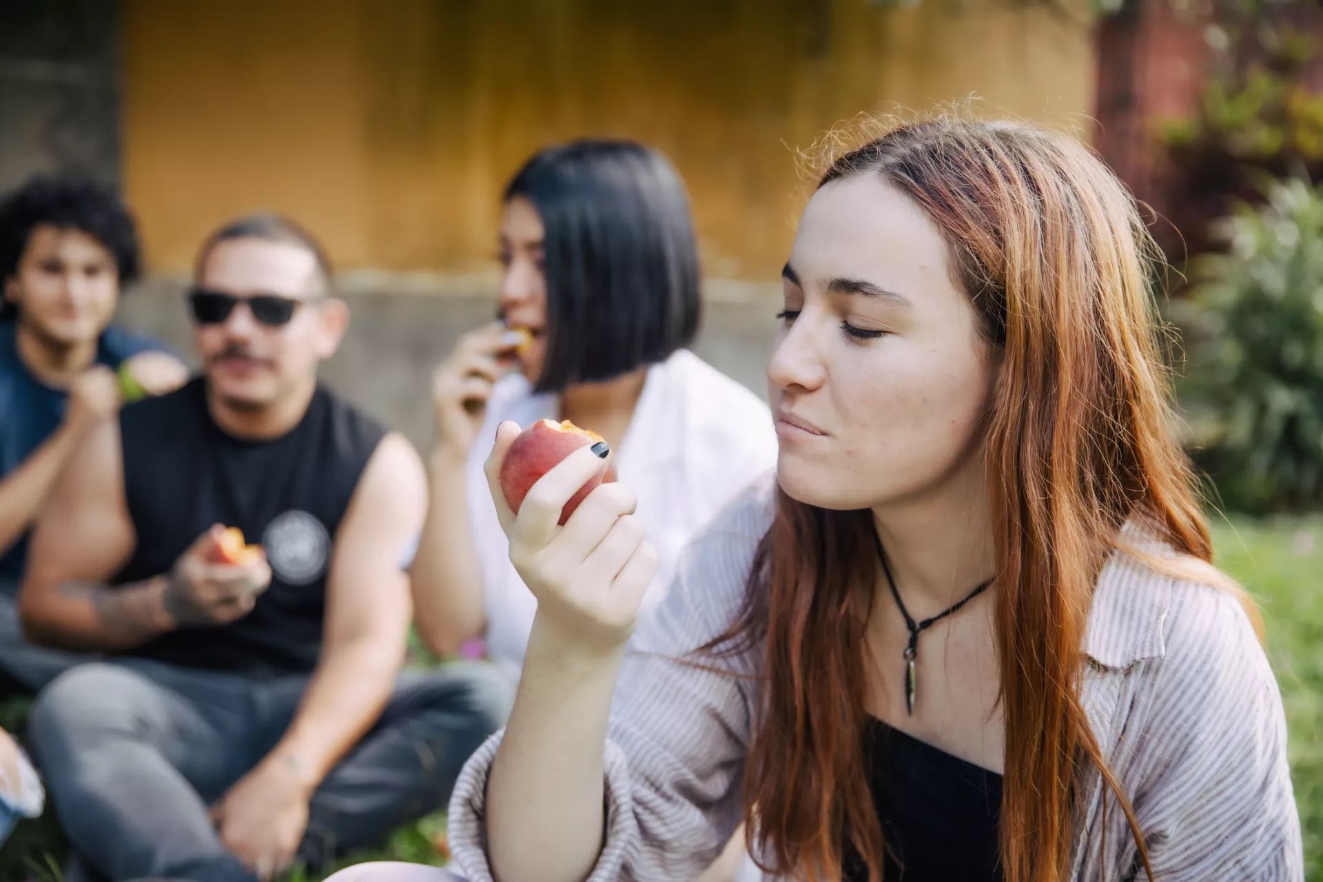 Adolescente mujer, comiendo manzana. Atr&aacute;s, se ven otros j&oacute;venes.