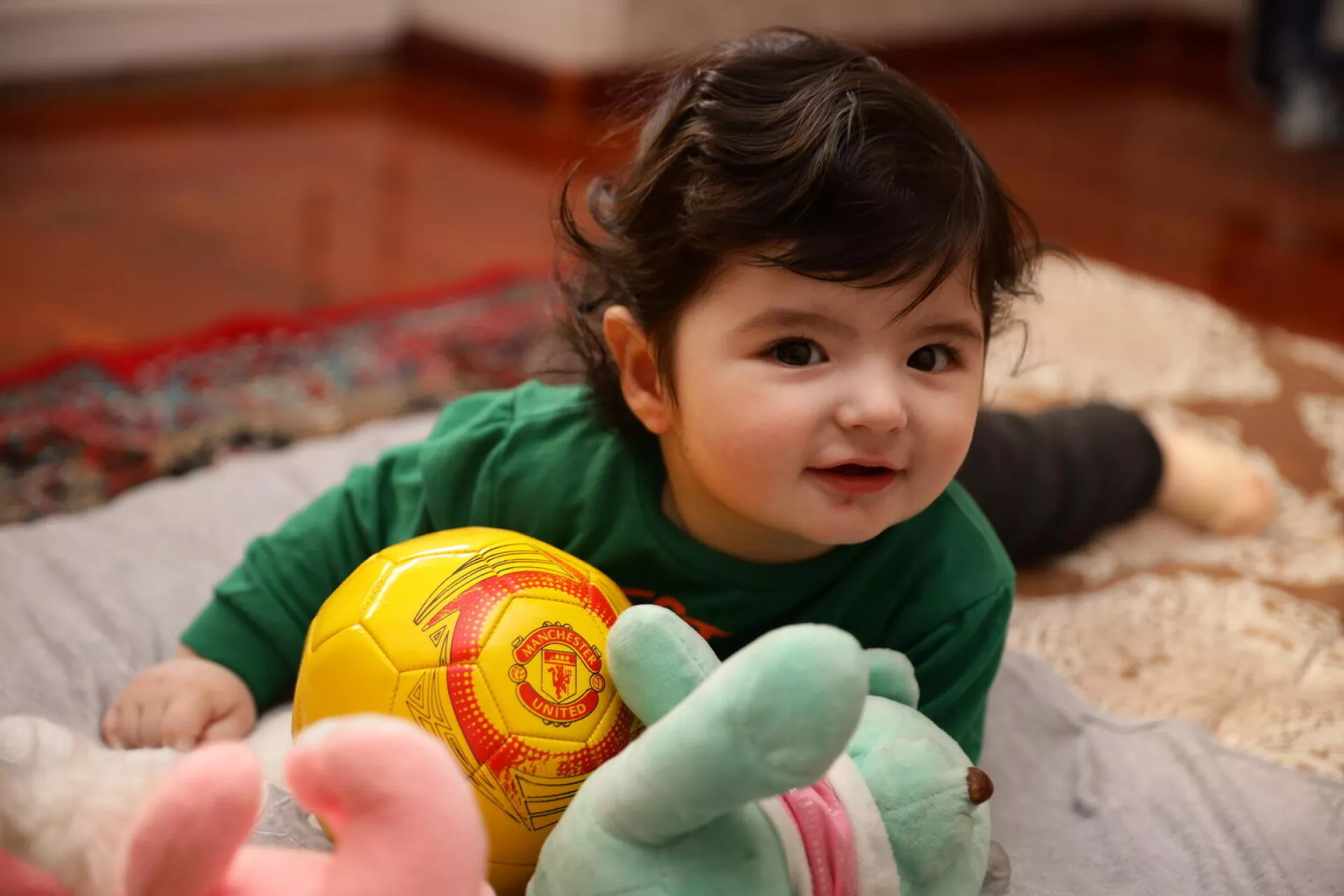 Ni&ntilde;a en el piso, con pelota de peluche y otros juguetes