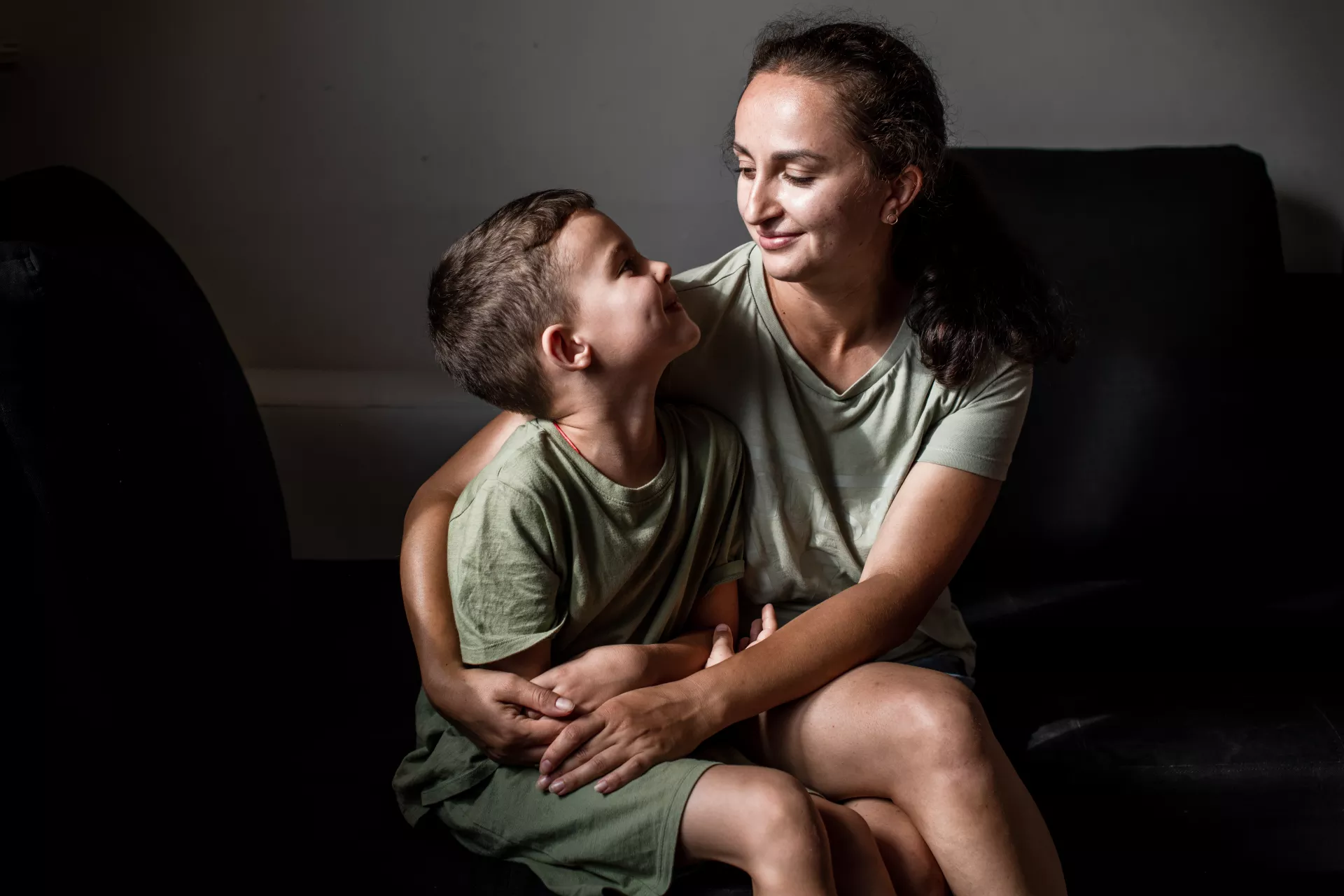 Mujer y ni&ntilde;o sentados al lado; la mujer abraza al ni&ntilde;o con ambos brazos.