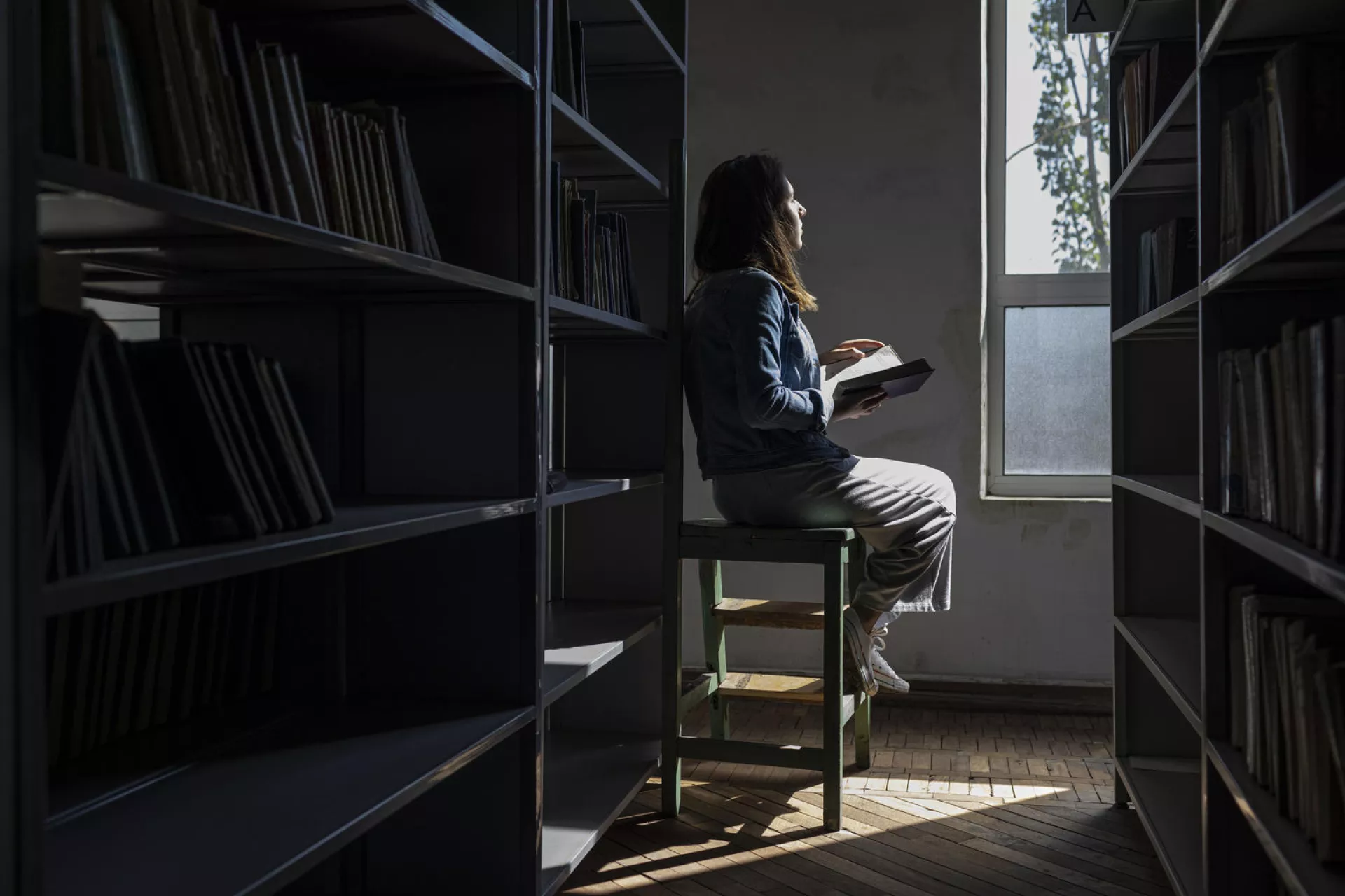 Adolescente sentada de espalda, a contra luz, mira por la ventana de una biblioteca