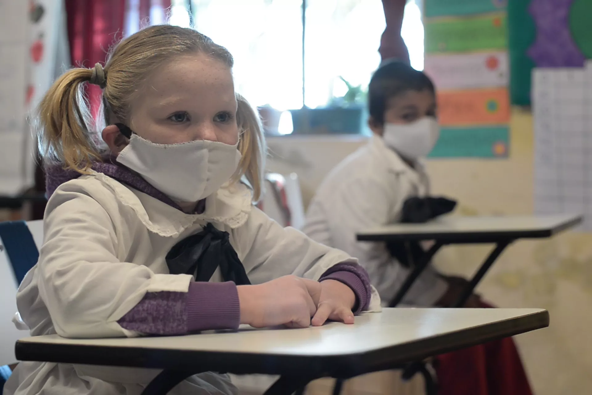 Una ni&ntilde;a y un var&oacute;n en un sal&oacute;n de clases, con tapabocas.