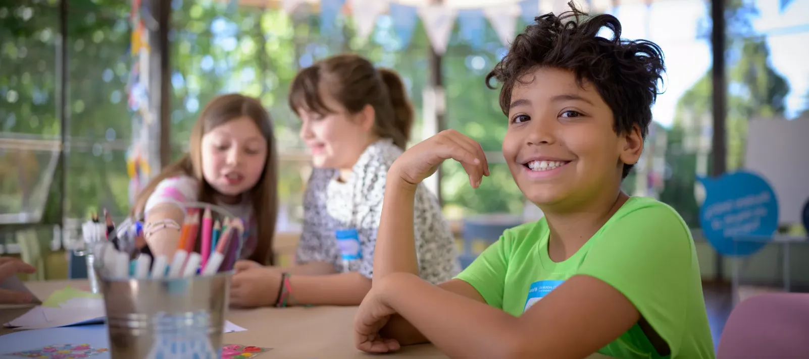 Tres ni&ntilde;os, uno sonriente y dos ni&ntilde;as escribiendo sus cartas en el fondo