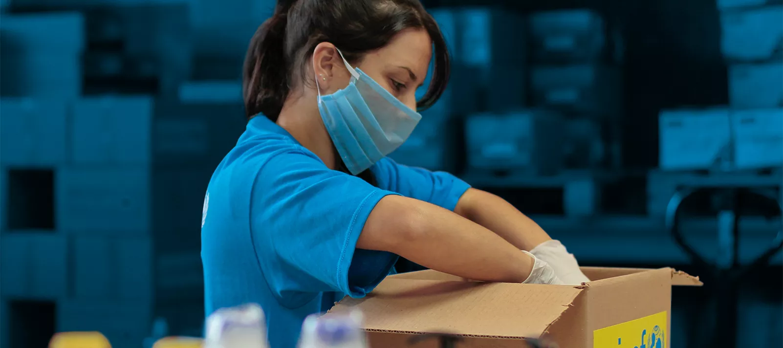 Mujer con remera de UNICEF y tapabocas armando caja con kit de higiene.