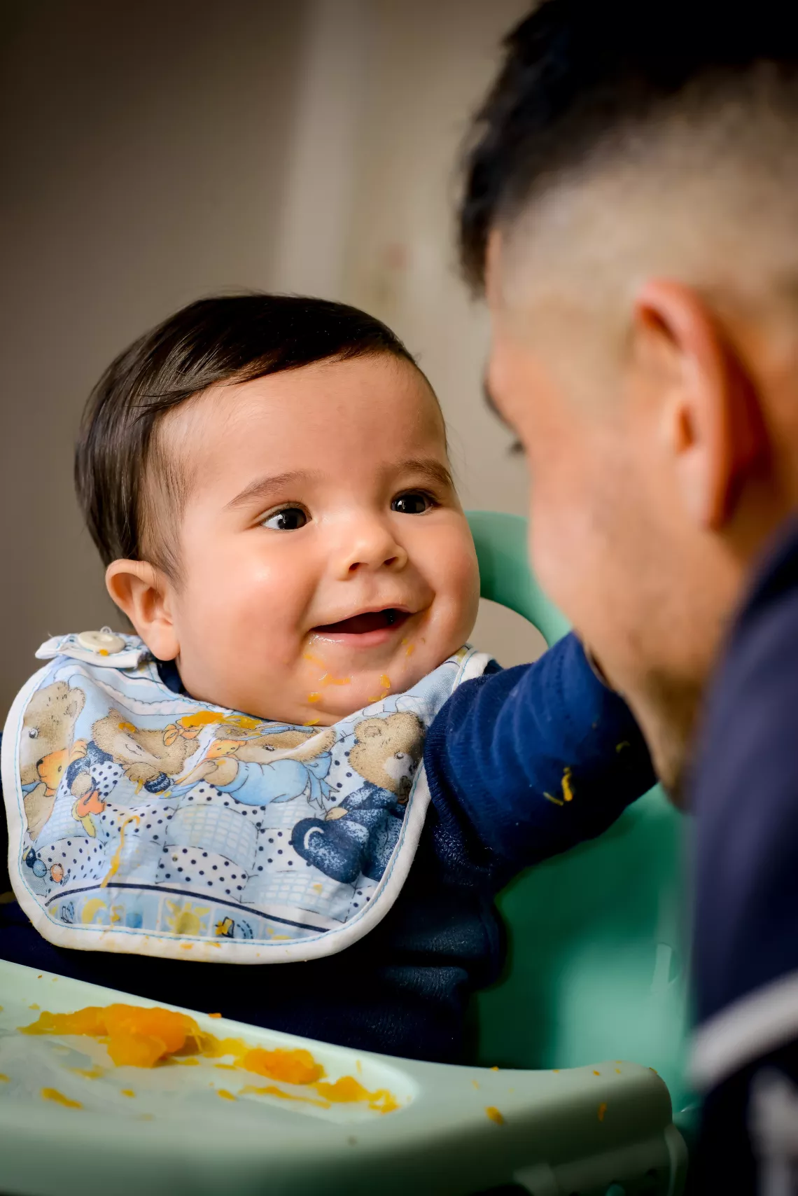 Beb&eacute; con babero mira y sonr&iacute;e a un hombre que se ve de perfil