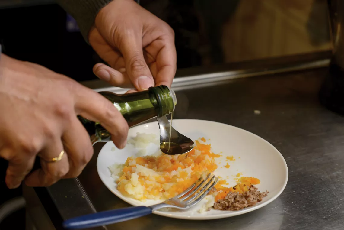 Manos sirviendo una cucharadita de aceite de oliva, sobre un plato con pur&eacute;.