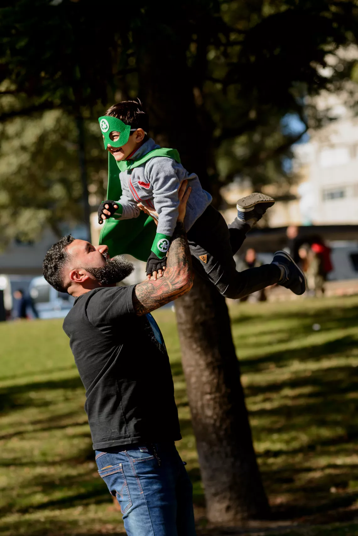 Ni&ntilde;o disfrazado, siendo alzado por un hombre, en un parque.