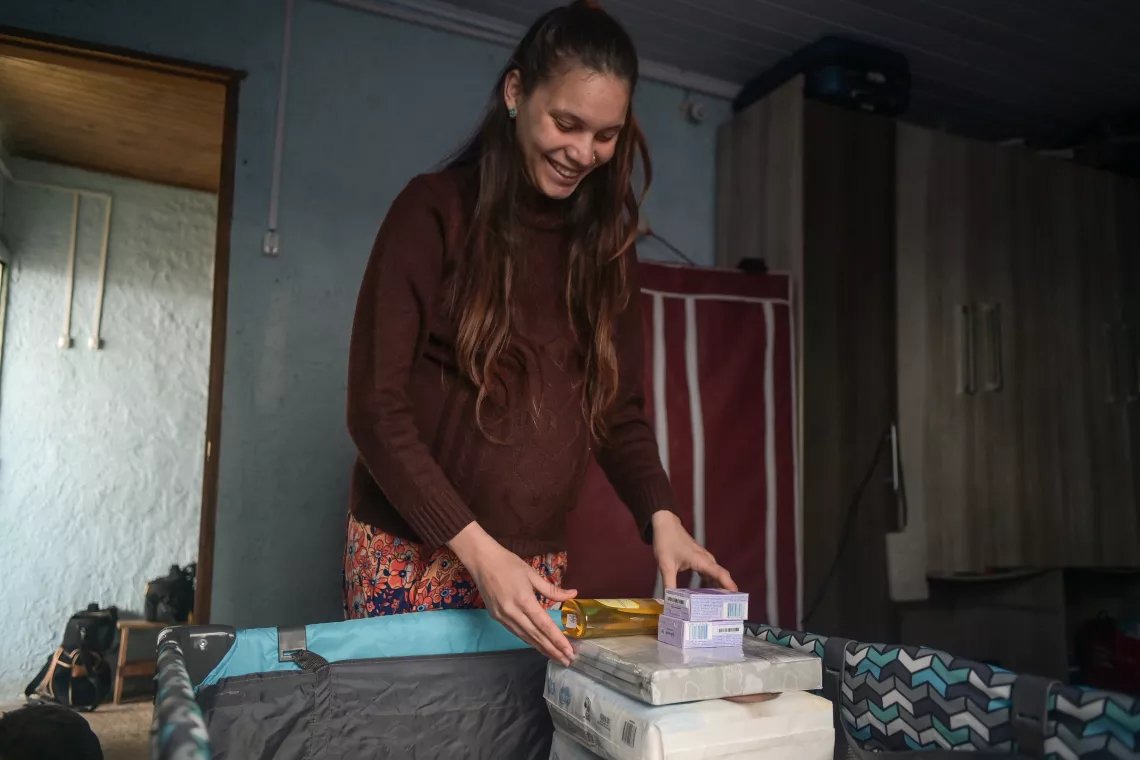 Mujer embarazada sonriendo, al lado de practicuna y productos para higiene del beb&eacute;.