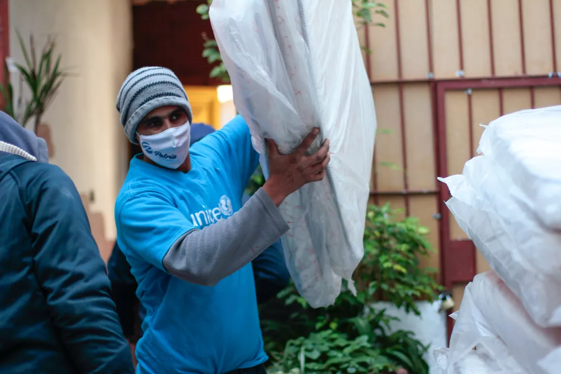 Hombre con camiseta de UNICEF, cargando colch&oacute;n de cuna.