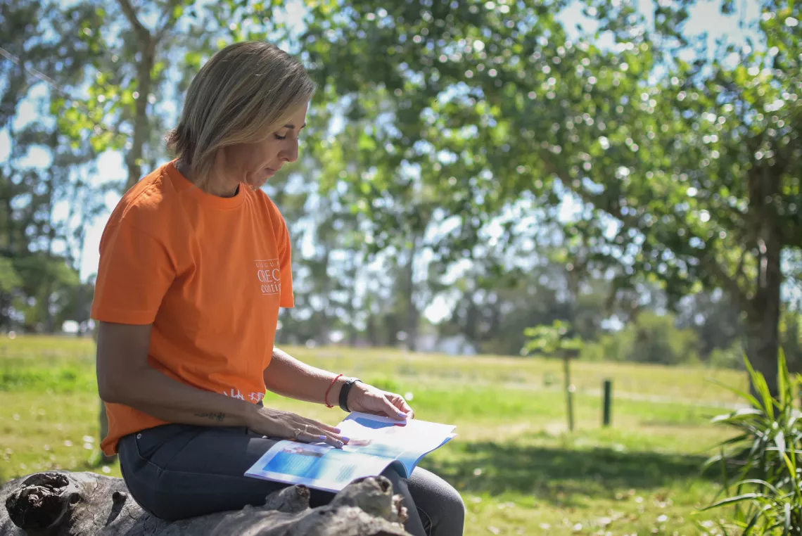 Mujer con remera anaranjada, sentada, leyendo gu&iacute;a.