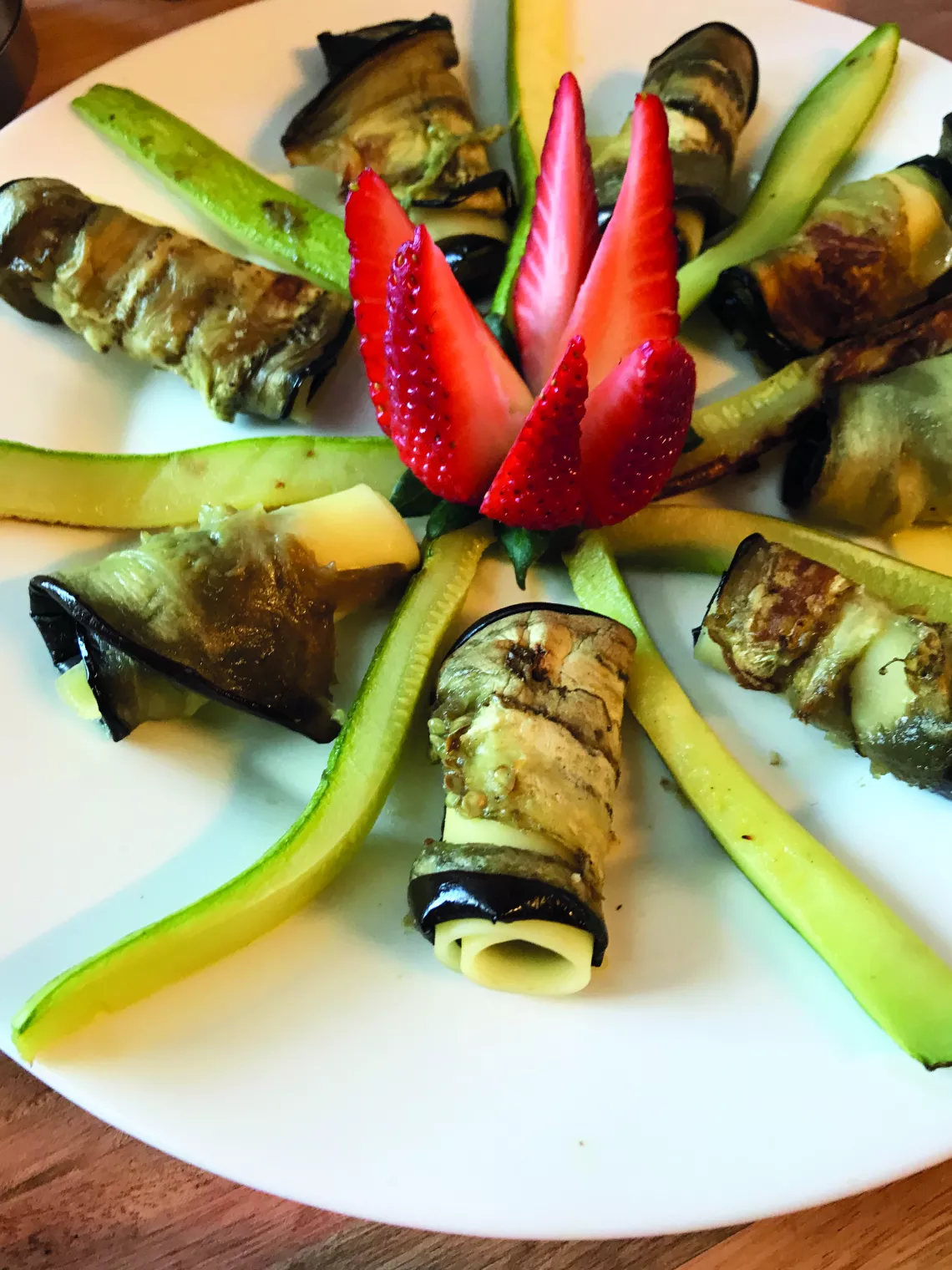 Rollitos de berenjena con verduras y ricotta. En el centro, hay una flor hecha con una frutilla.