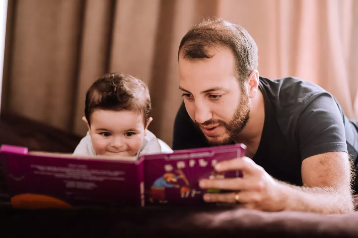 Hombre leyendo un libro con un ni&ntilde;o de menos de un a&ntilde;o.