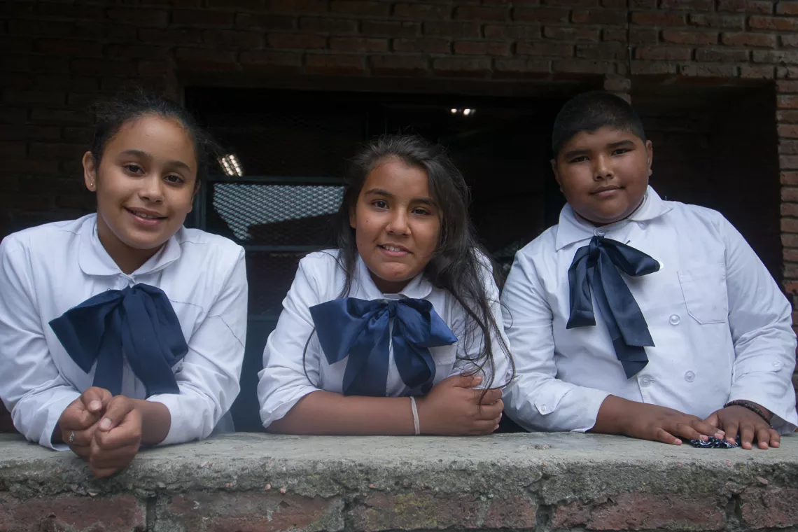Tres compa&ntilde;eros de clase de Melina miran a c&aacute;mara en la escuela