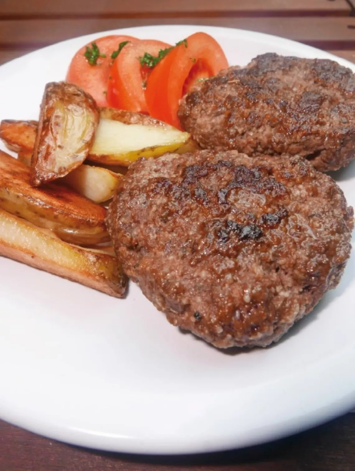 Dos hamburguesas caseras en un plato con tomate y papas al horno.