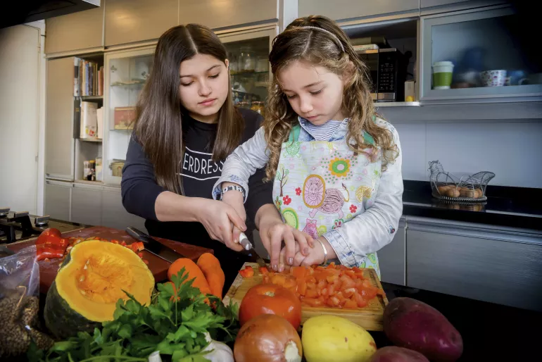 2 ni&ntilde;as pican verduras en la cocina de su casa