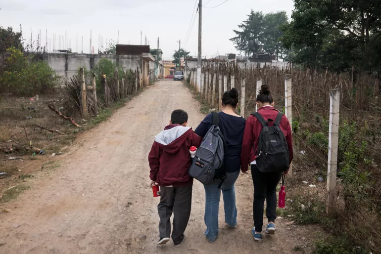 Una mujer y sus dos hijos caminan en un camino de tierra en Guatemala