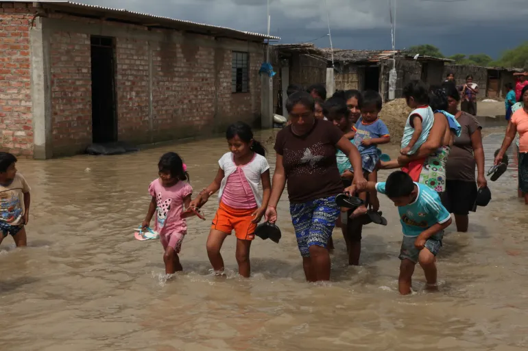 Calle inundada; mujeres y ni&ntilde;os avanzan entre el agua turbia.
