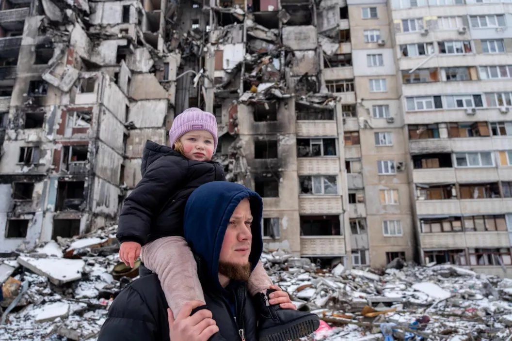Un hombre camina con su ni&ntilde;a en hombros frente a edificios derrumbados por el bombardeo