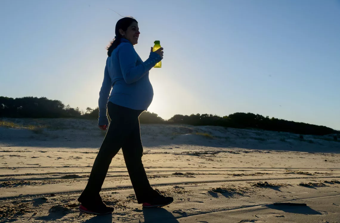 Mujer embarazada caminando en la playa con botella de agua