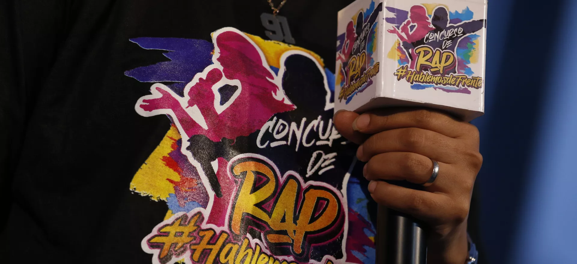 animador del evento de premiaci&oacute;n del concurso de rap Hablemos de frente sostiene micr&oacute;fono mostrando el logotema del concurso