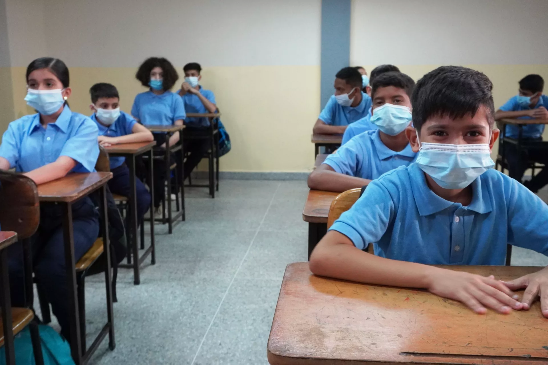 Ni&ntilde;os y ni&ntilde;as sentados en un sal&oacute;n de clases con tapabocas