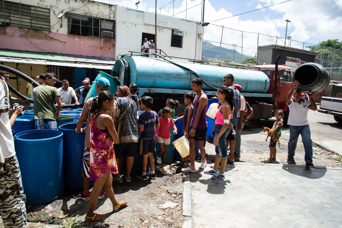Las familias se congregan con sus bidones alrededor de los camiones cisterna en Petare, Caracas.