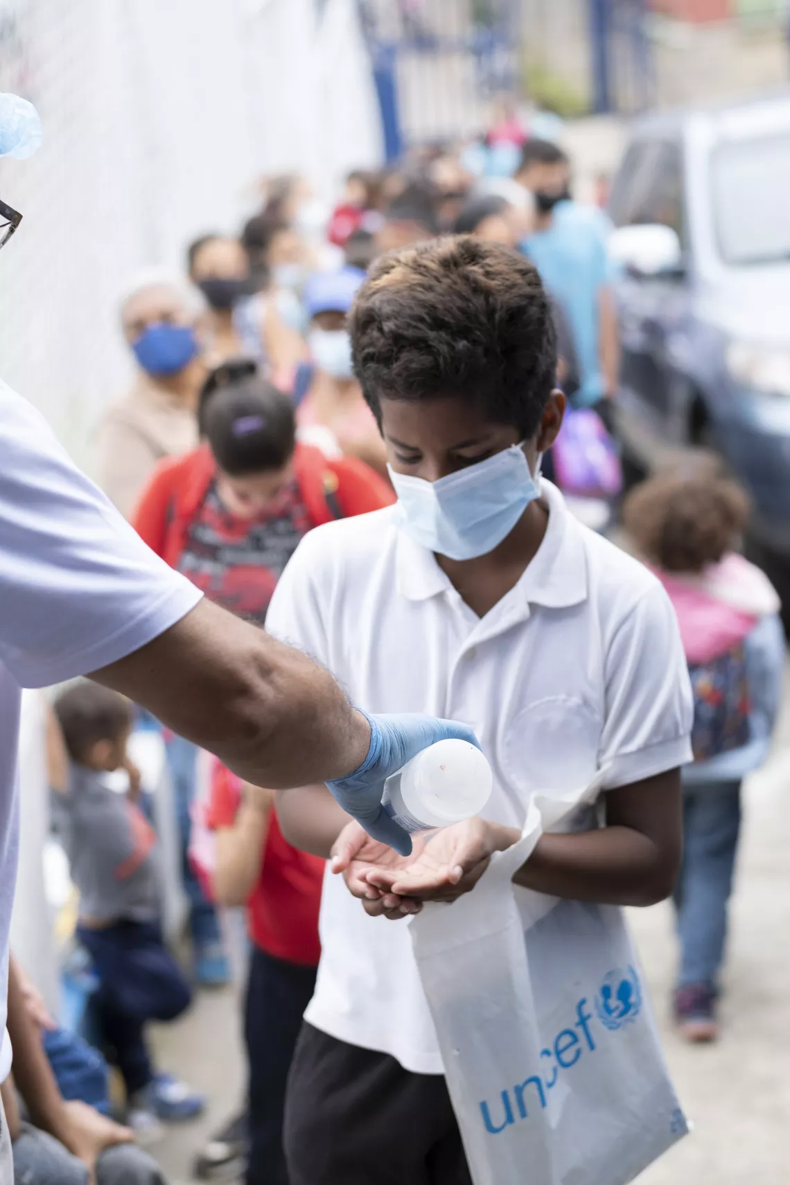 Abraham receives antibacterial gel before entering school. He also carries with him some of the materials from the school kit that UNICEF provided to support the return to school.