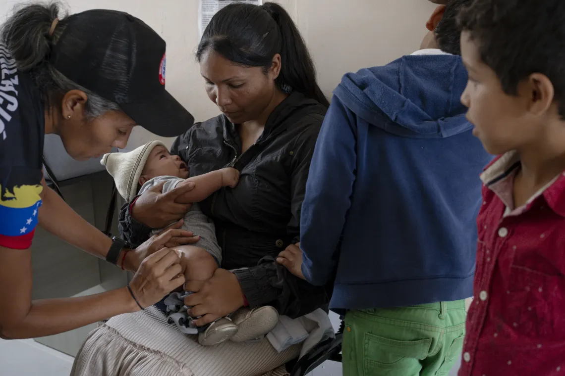A baby receives a vaccine while held by his mother during a visit by a primary health care team.