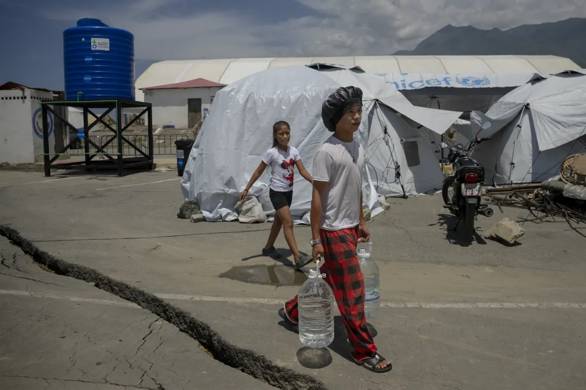 Derwimar, de 9 a&ntilde;os, camina junto a su hermano mientras &eacute;l transporta recipientes con agua por el campamento temporal donde vive su familia.