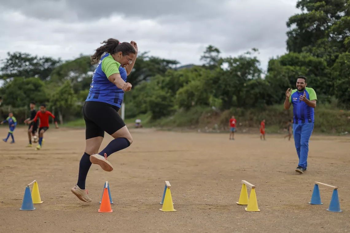Emma Mill&aacute;n voluntaria de C&aacute;ritas Car&uacute;pano e integrante del equipo de madres de Misericordia F.C., salta obst&aacute;culos mientras el entrenador Robert Rojas la alienta a continuar.
