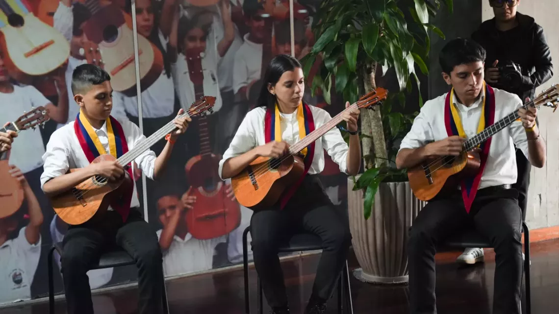 Dos ni&ntilde;os y una ni&ntilde;a, integrantes de El Sistema tocan cuatro sentados en una silla durante una muestra musical en el acto de ratificaci&oacute;n de El Sistema como Embajador Nacional de UNICEF