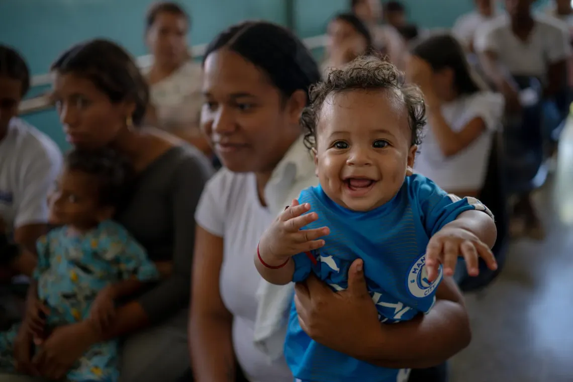 A young child smiles while being held by a woman in the waiting area during a UNICEF-supported health outreach session in Santa Luc&iacute;a del Tuy, Miranda State, Venezuela.