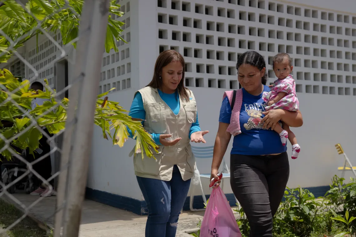 Zulay Gonz&aacute;lez, oficial de Nutrici&oacute;n de UNICEF Venezuela, camina junto a Anderbis Acosta, quien lleva en brazos a su hija de nueve meses, a las afueras del centro de salud en Santa Luc&iacute;a del Tuy, estado Miranda, Venezuela.