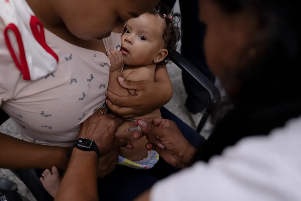 A health worker vaccinates a young child held by a caregiver during a UNICEF-supported health outreach session in Santa Luc&iacute;a del Tuy, Miranda State, Venezuela.