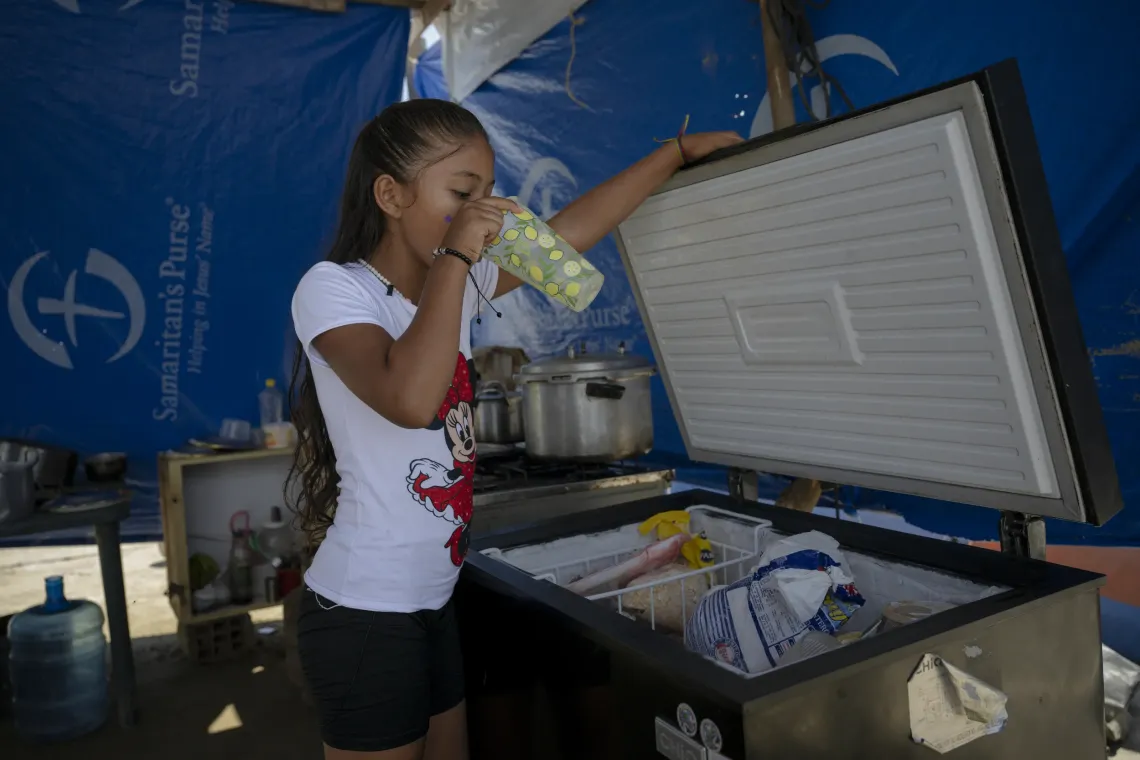 Derwimar, 9, drinks water that her family keeps in a refrigerator salvaged from their former apartment at the temporary camp in Mare Abajo.