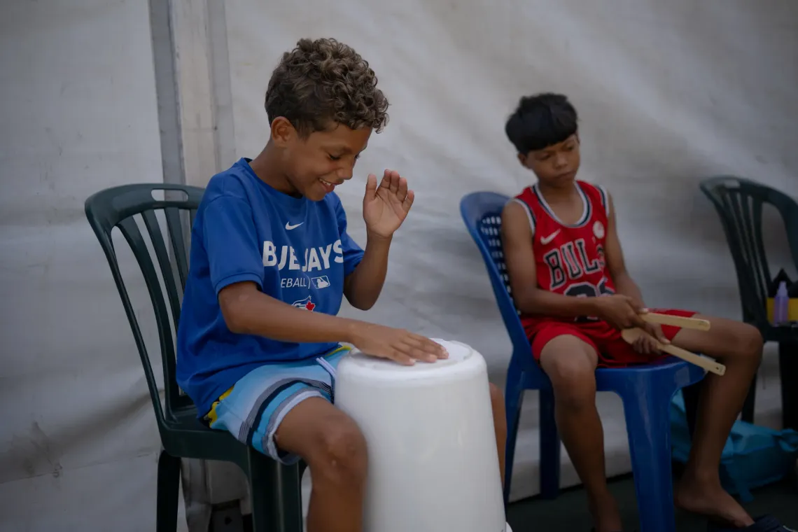 Dami&aacute;n, 13, uses a plastic container as alongside a friend at the temporary camp where he lives in La Guaira, Venezuela.