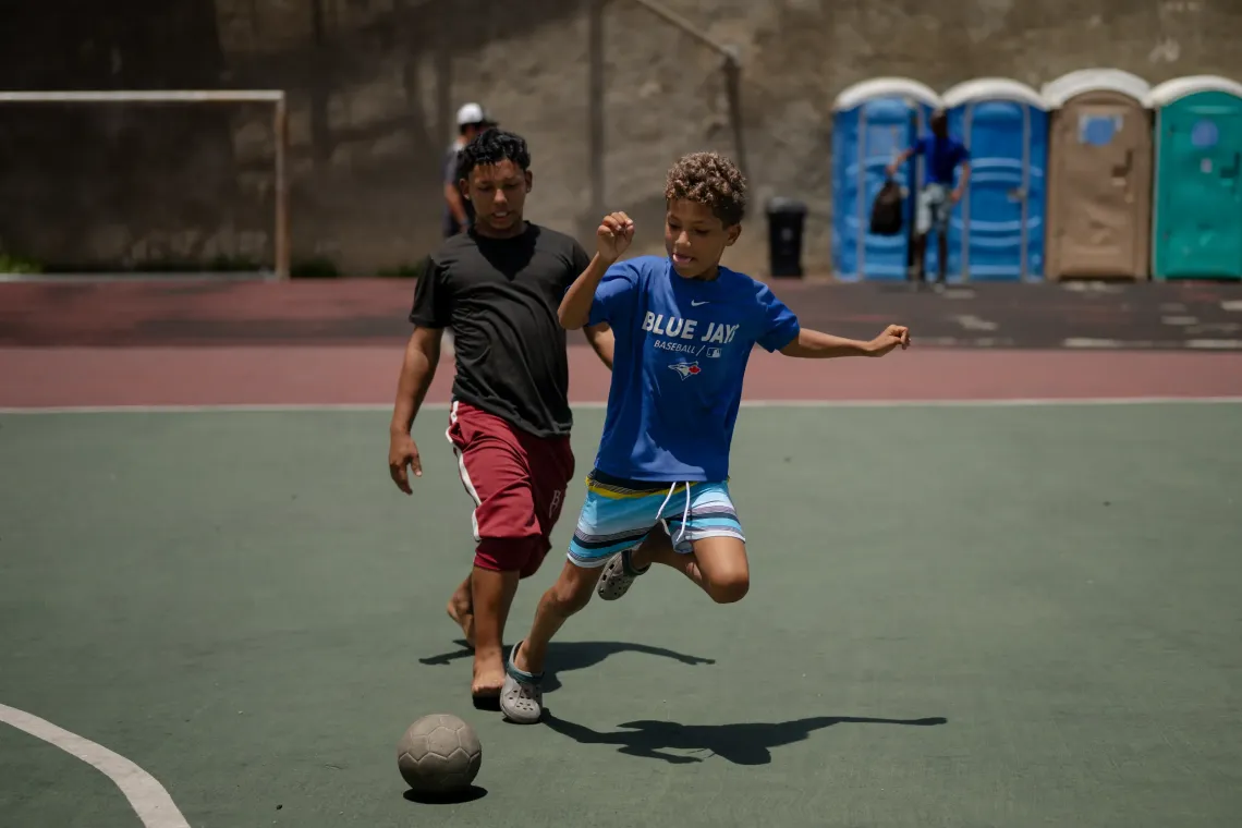 Dami&aacute;n, 13, plays football with another boy at the Jos&eacute; Mar&iacute;a Vargas sports complex in La Guaira, where he lives with his family in a temporary camp.