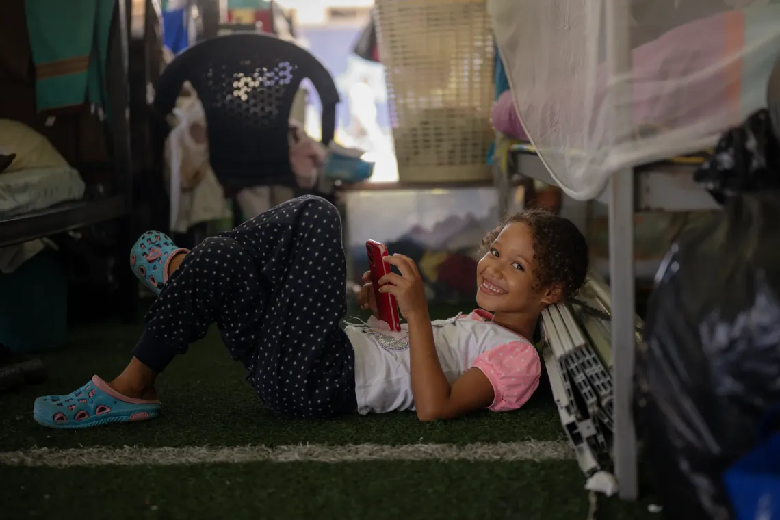 Mercy, 12, one of Dami&aacute;n&rsquo;s cousins, relaxes with a phone at the temporary camp in the Jos&eacute; Mar&iacute;a Vargas sports complex in La Guaira, where she lives with her family.