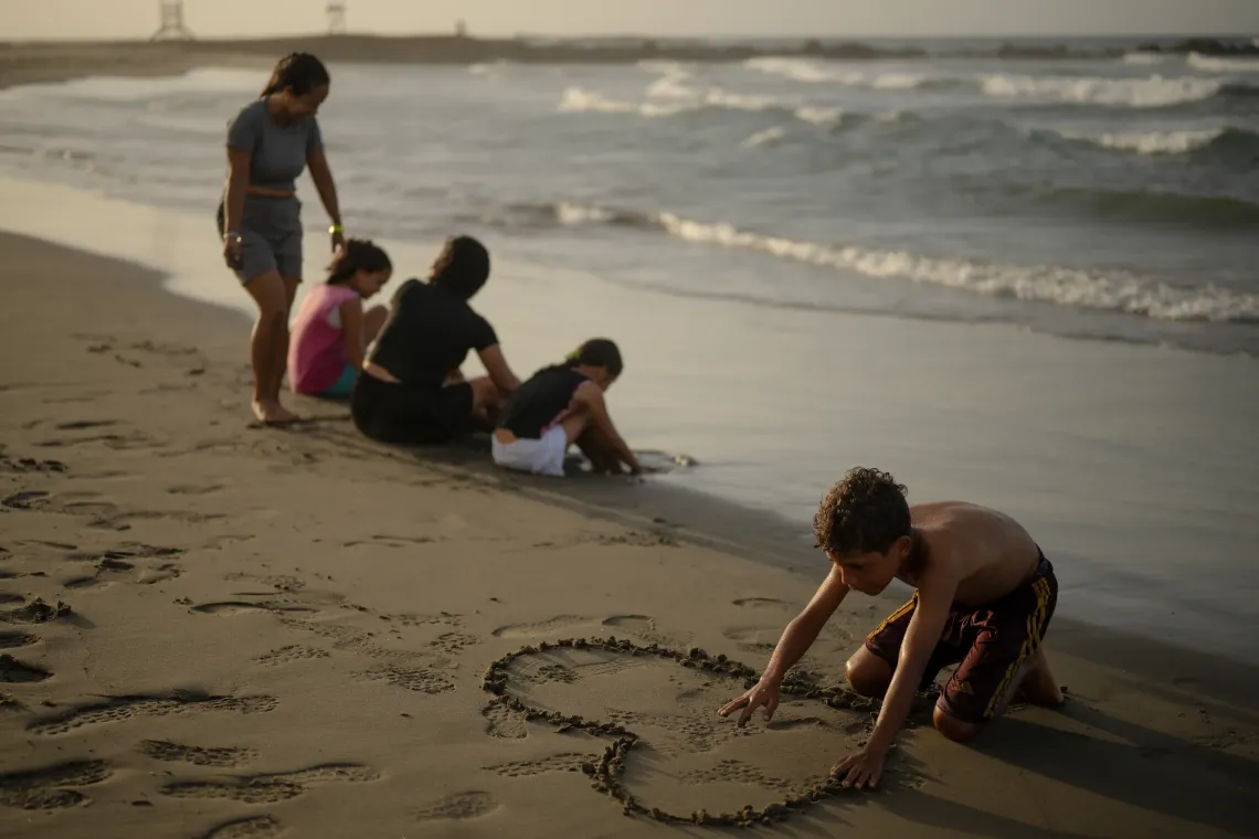 Dami&aacute;n, 13, draws a heart in the sand while his aunt Mercedes and other family members spend time by the sea in La Guaira, Venezuela.