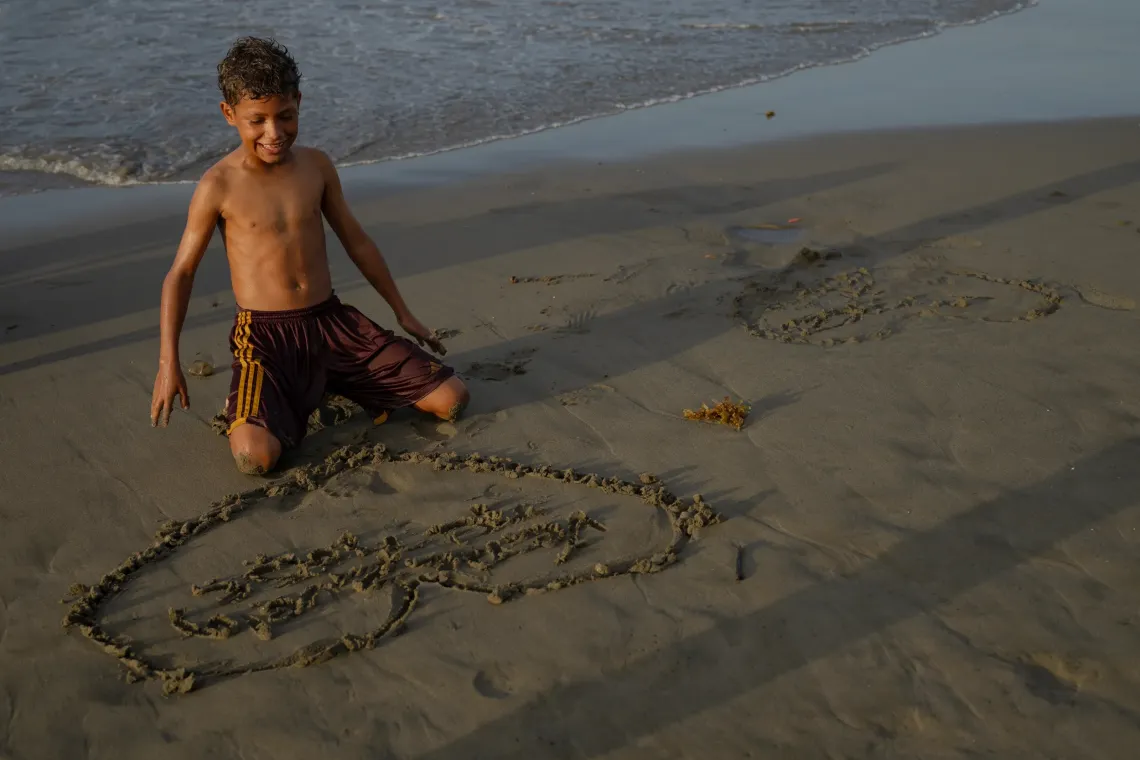 Dami&aacute;n, 13, smiles beside the heart he has drawn in the sand on a beach in La Guaira, Venezuela.