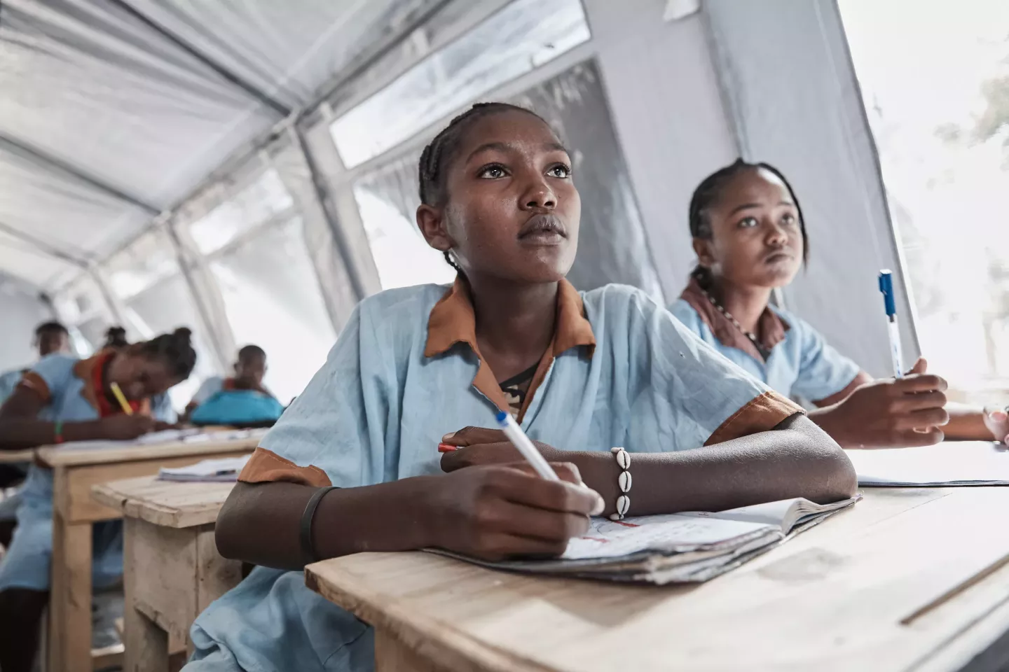 Two girls in Madagascar work at a desk in a temporary classroom following Cyclone Freddy.